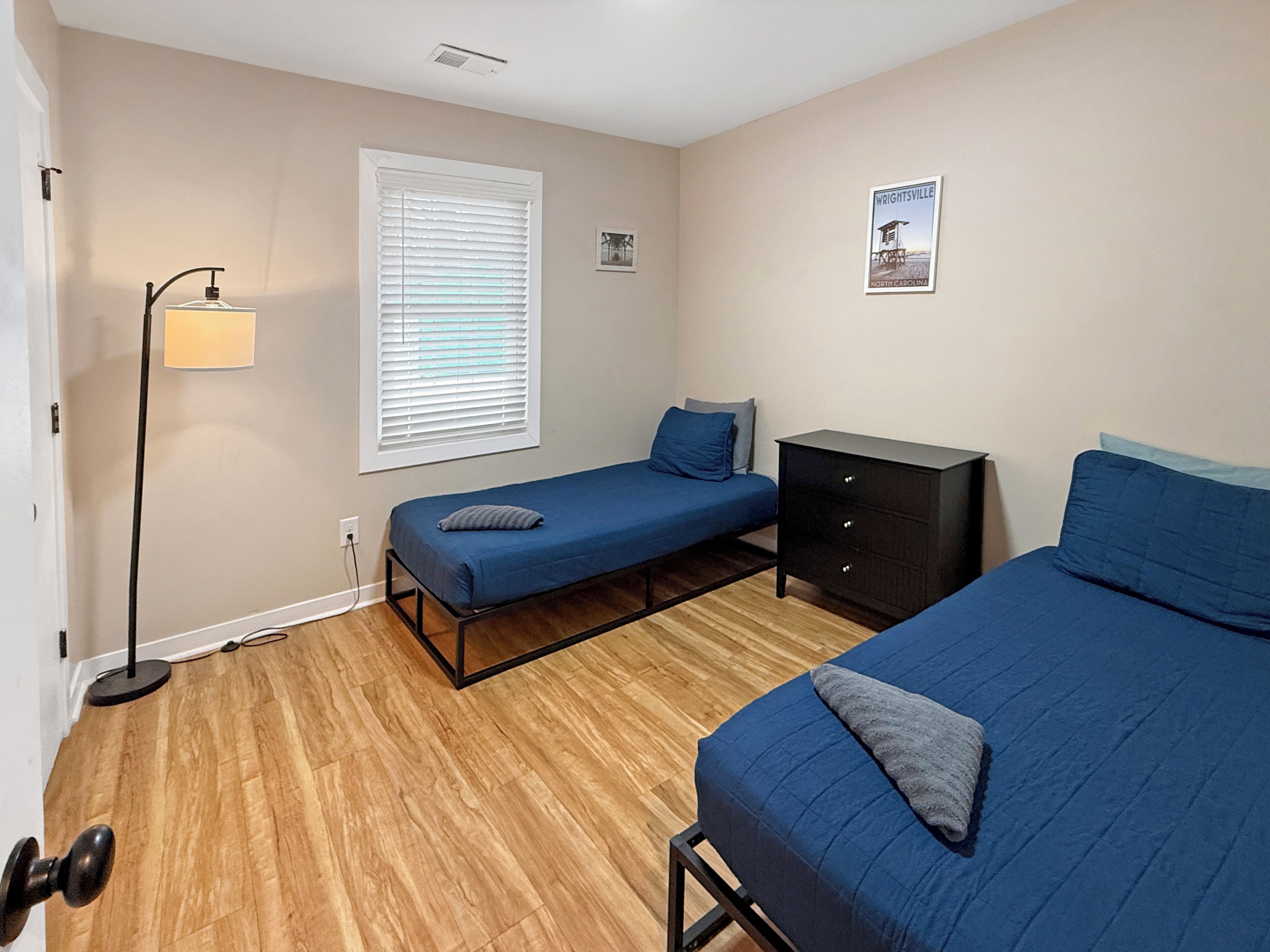 A bedroom with two beds, a nightstand, a lamp, and a window with blinds.