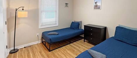 A bedroom with two beds, a nightstand, a lamp, and a window with blinds.