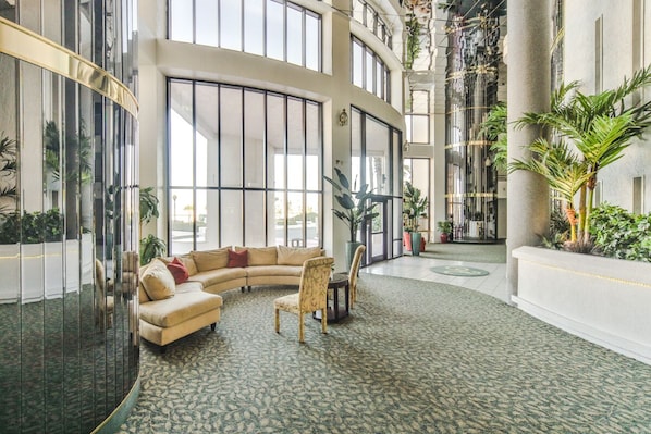 A spacious lobby with a curved sofa, chairs, and a coffee table. Large windows and a high ceiling with decorative elements are visible. - Direct Oceanfront 3BR/3BA Incredible Views & Condo! (Daytona Beach Shores)