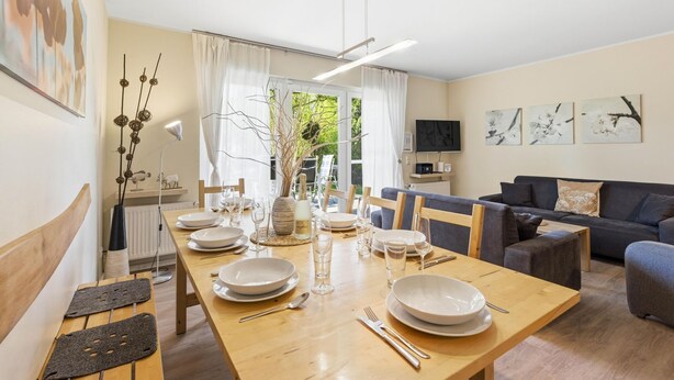 Ein Essbereich mit einem Holztisch, gedeckt für vier Personen, einer Couch und einem Fernseher an der Wand.