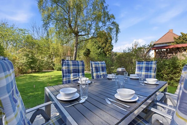 A wooden table set outdoors with plaid cushions, a pot, and glassware.