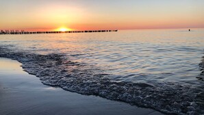 Ein Strand bei Sonnenuntergang mit Wellen, einem Steg und einer Person im Wasser.
