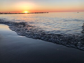 A beach at sunset with waves, a pier, and a person in the water.
