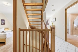 A modern interior with a wooden staircase, a bed, and a bathroom with a glass shower.