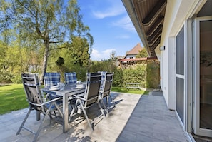 Un patio al aire libre con una mesa y sillas, una pérgola de madera y una vista de una casa al fondo.