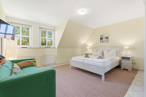 A bedroom with a bed, two bedside tables, a window, and a radiator.