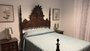 Ein Schlafzimmer mit hölzernem Kopfteil, einem Bett mit Steppdecke, einem Nachttisch mit Lampe, einer Kommode und gerahmten floralen Kunstwerken an den Wänden.