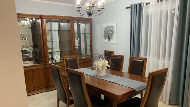 Ein Esszimmer mit Holztisch, sechs Stühlen, einer Blumenvase, einem Kronleuchter und einem Glaskabinett.