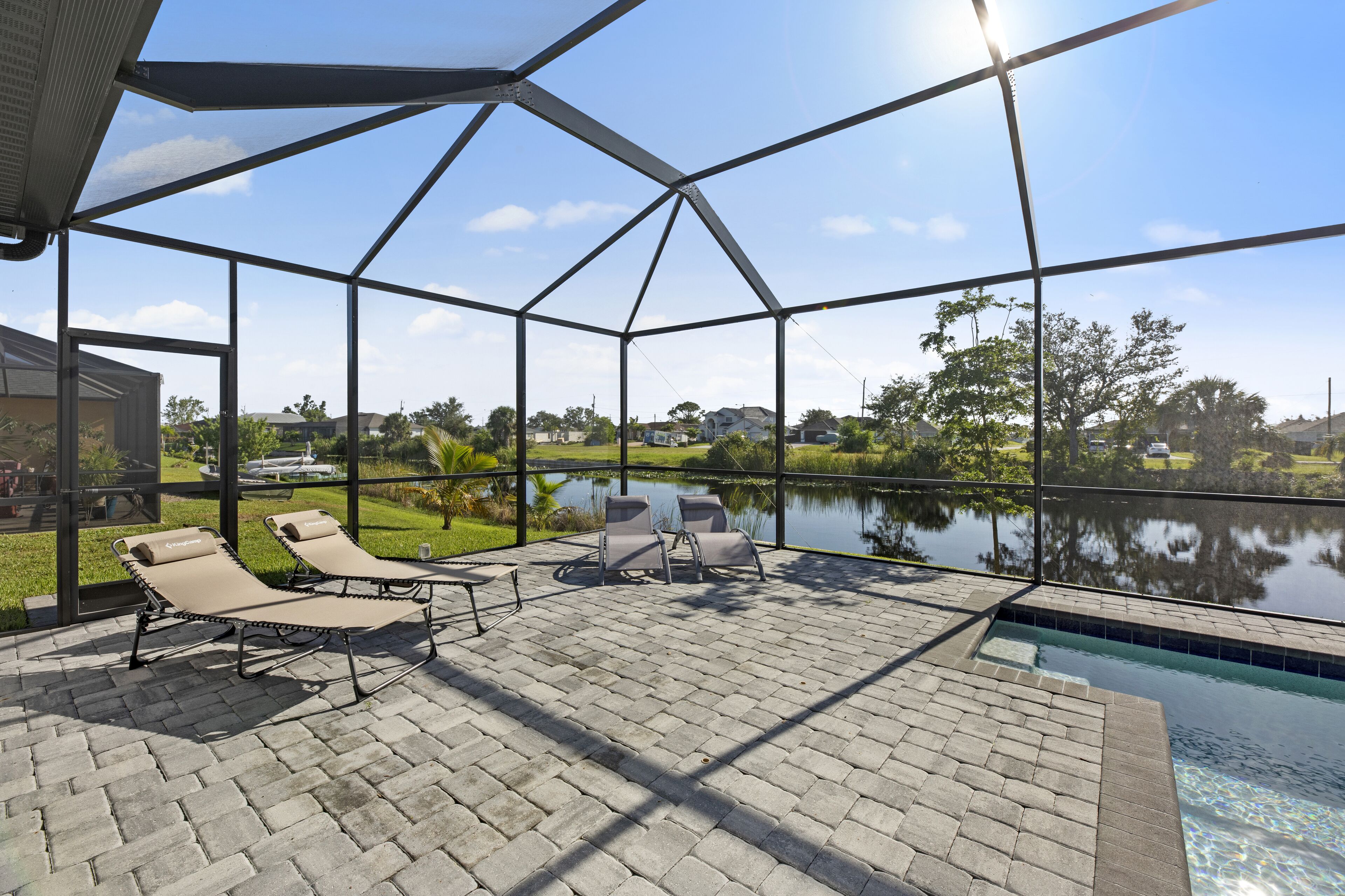 Une terrasse extérieure ensoleillée, dotée de chaises longues, d’une piscine et offrant une vue sur un lac et la verdure environnante.