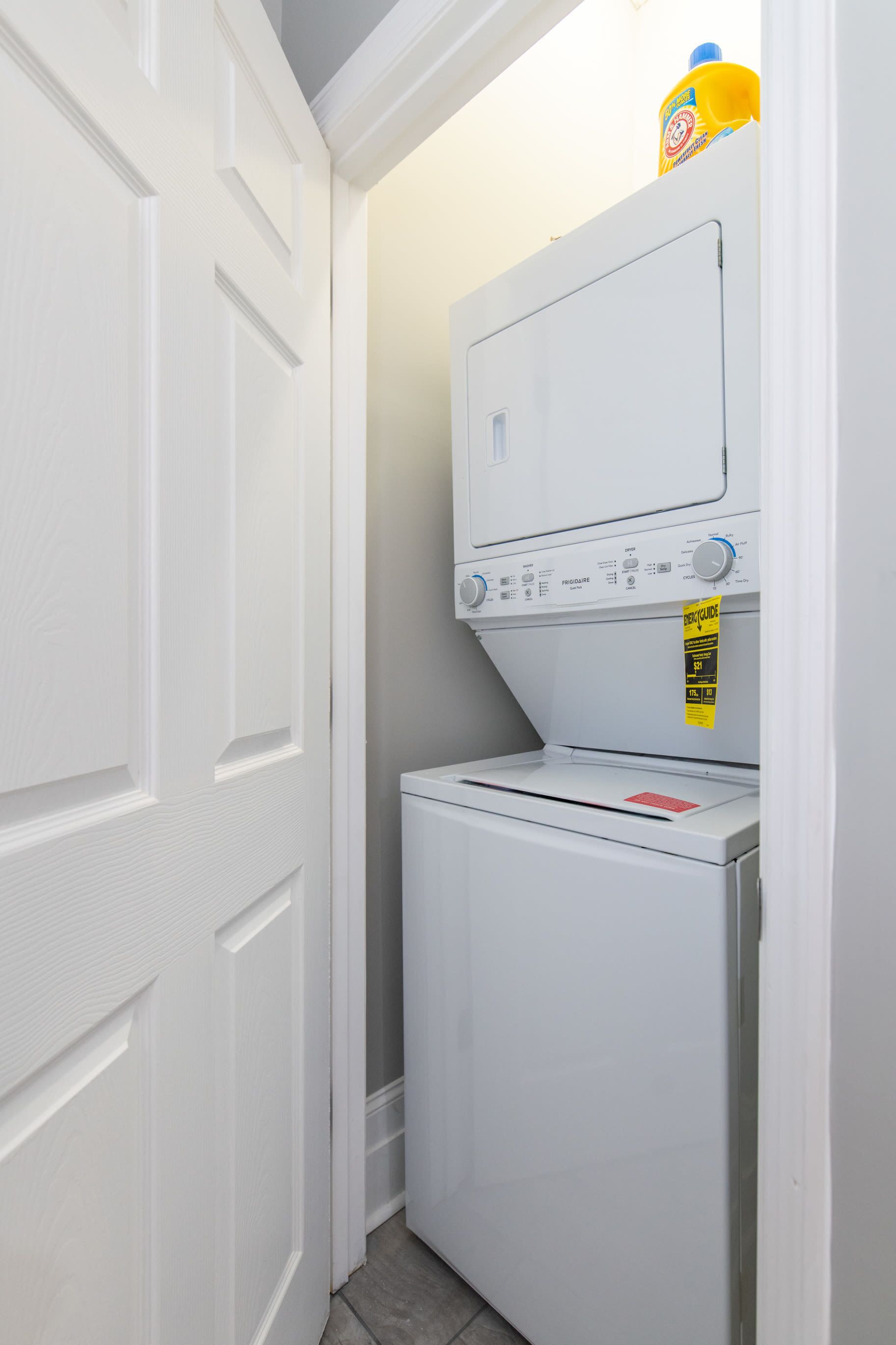 A laundry room with a front-loading washer and dryer, a yellow caution sign, and a bottle of detergent on top of the dryer.