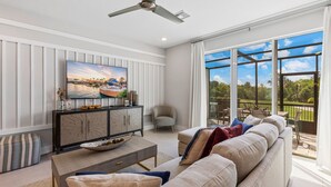 A modern living room with a large TV, comfortable seating, and a balcony with a view.