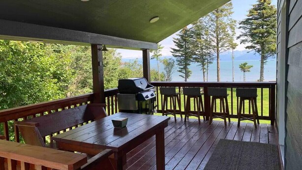 Eine Holzterrasse mit Grill, Sitzgelegenheiten und Blick auf den See.