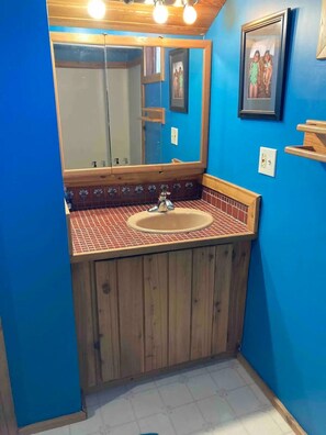 A bathroom with a wooden vanity, a large mirror, and a tiled backsplash.