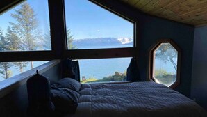 Ein Schlafzimmer mit einem großen Bett, einem Fenster und Blick auf einen See und Berge.