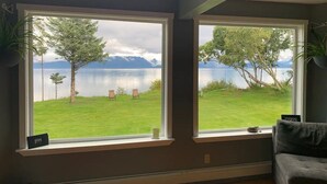 Ein Zimmer mit zwei großen Fenstern, das Blick auf eine Wiese und ein Gewässer mit Bergen in der Ferne bietet.
