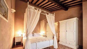 Ein Schlafzimmer mit Himmelbett, Nachttisch, Kleiderschrank und Fliesenboden.