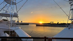 Uma marina com barcos atracados, um pôr do sol ao fundo e um cais que se estende sobre a água.