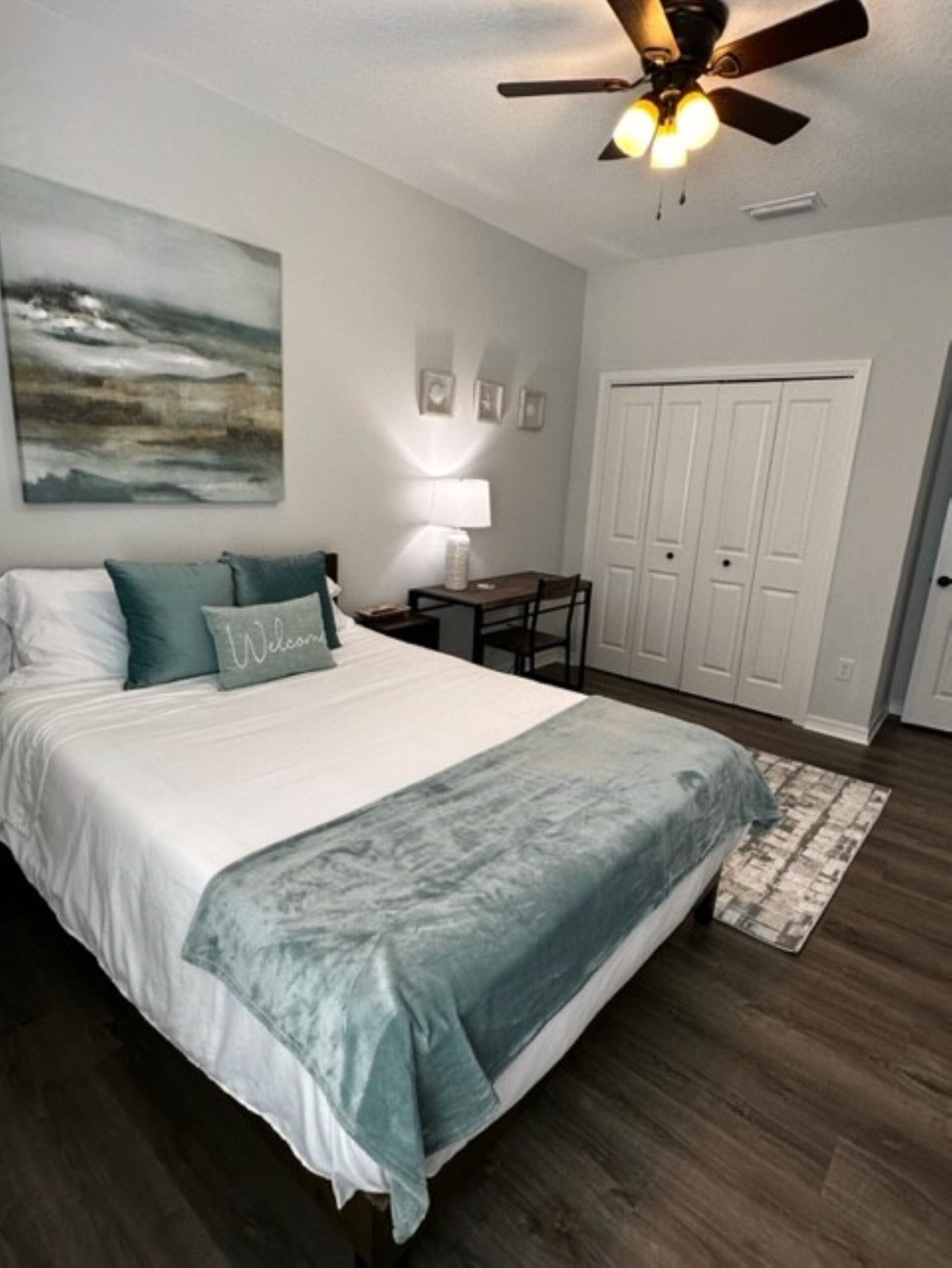 A bedroom with a bed, a ceiling fan, a desk, and a chair.