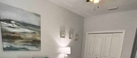 A bedroom with a bed, a ceiling fan, a desk, and a chair.