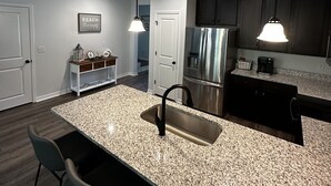 Cozinha moderna com bancadas de granito, eletrodomésticos de aço inoxidável e iluminação pendente.
