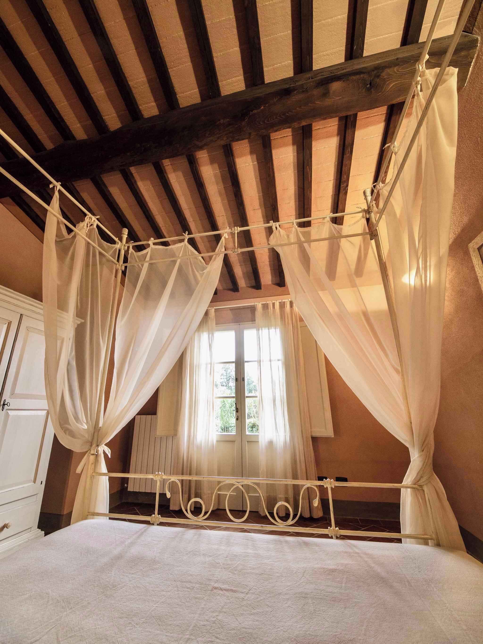 Una camera da letto con un letto a baldacchino, travi in legno al soffitto e tende leggere.