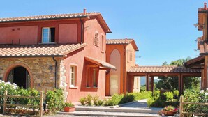 Um edifício tradicional em estilo mediterrâneo, com entrada em arco de pedra, telhado em azulejos e um jardim com plantas e flores em vasos.