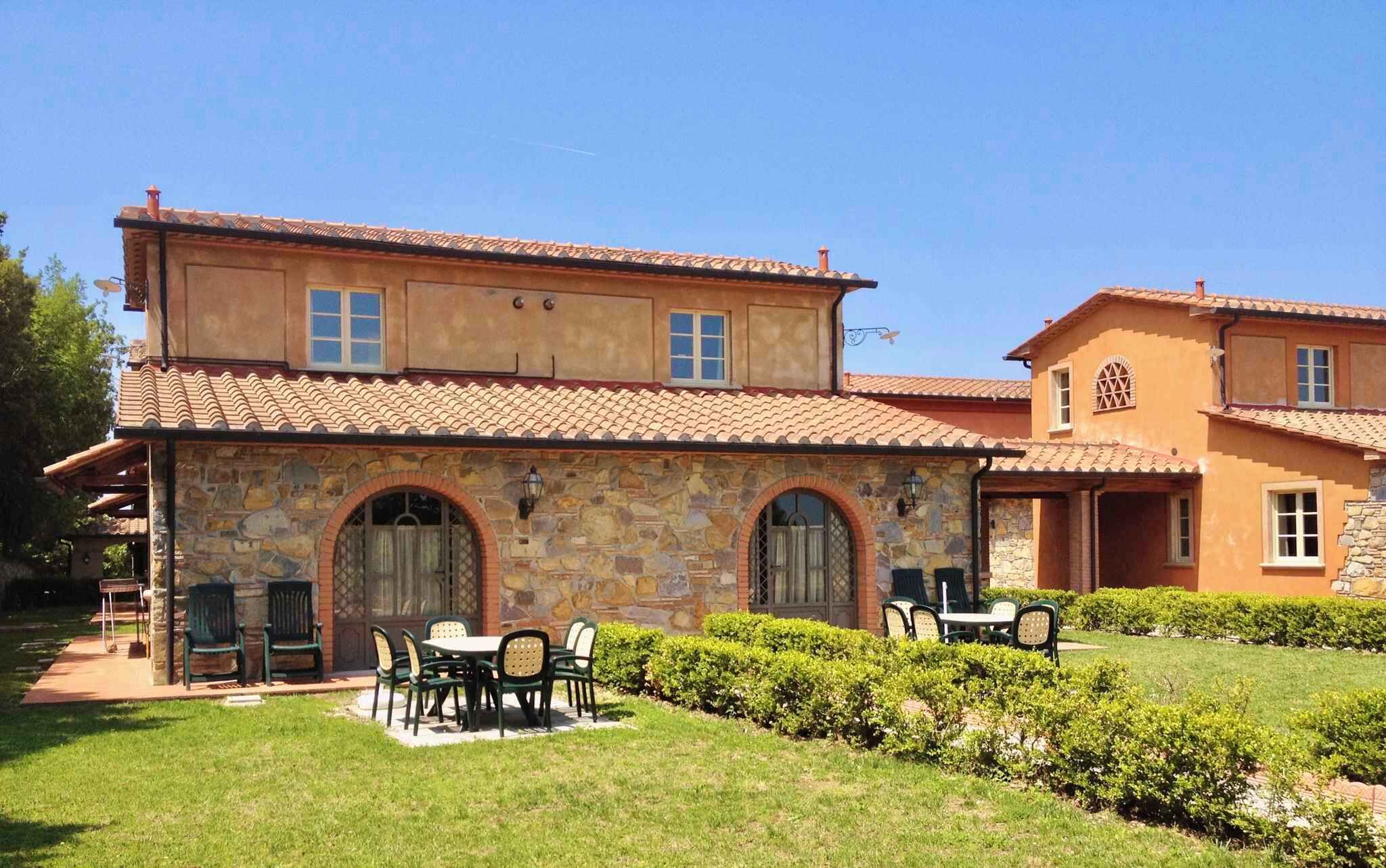 A two-story stone building with a tiled roof, outdoor seating area, and well-maintained hedges.