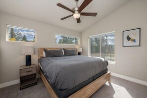 Une chambre à coucher avec un lit, deux tables de chevet, un ventilateur de plafond et des fenêtres donnant sur la forêt.
