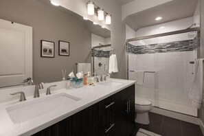 A modern bathroom with a double sink, a toilet, a shower area, and a large mirror.