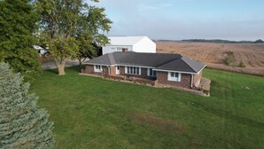 A single-story house with a brick exterior and a dark roof, surrounded by a well-maintained lawn and a large tree to the left.