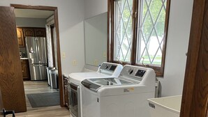 A laundry room with a front-loading washer and dryer, wooden flooring, and a view through a window.