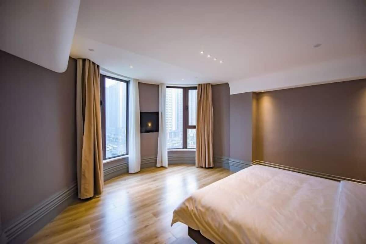 A modern hotel room with a large bed, a flat-screen TV, and a city view.