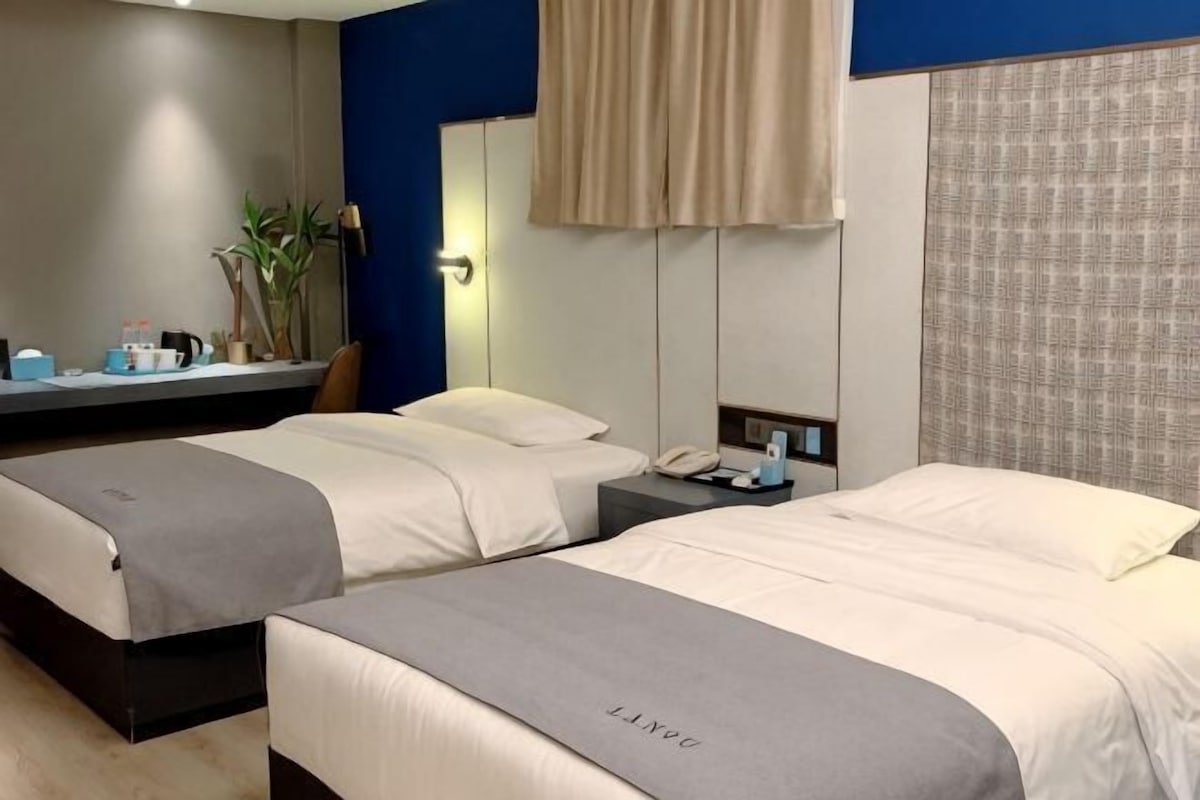 Habitación de hotel con dos camas, una mesita de noche con lámpara, un espejo y una ventana con cortinas.