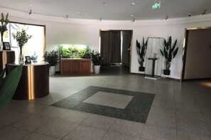 Eine Hotelhalle mit einer Rezeption, einer grünen Wand mit Pflanzen und einem gefliesten Boden.