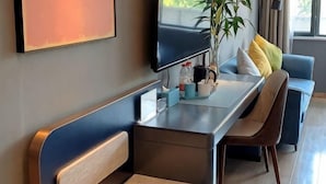 Habitació d'hotel moderna amb un sofà, una taula de dinar, una televisió i una planta.