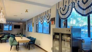 A dining area with a long table and chairs, a refrigerator, and a television on the wall.