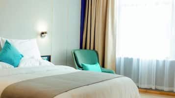 Ett hotellrum med en stor säng, en grön fåtölj och utsikt över omgivningarna genom tunna gardiner.
