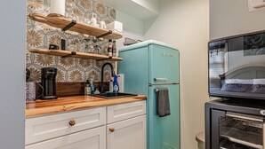 Eine Küche mit einem türkisblauen Kühlschrank, einer Holz Arbeitsplatte, weißen Schränken und einer gemusterten Spritzschutzwand.
