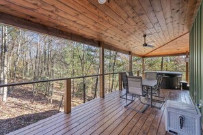 A covered outdoor deck with a table and chairs, a grill, and a view of a forest. - Anchor Point- Hot Tub, Firepit, Ping Pong (Rogers)