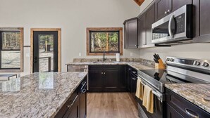 A modern kitchen with dark cabinets, granite countertops, and stainless steel appliances. - Anchor Point- Hot Tub, Firepit, Ping Pong (Rogers)
