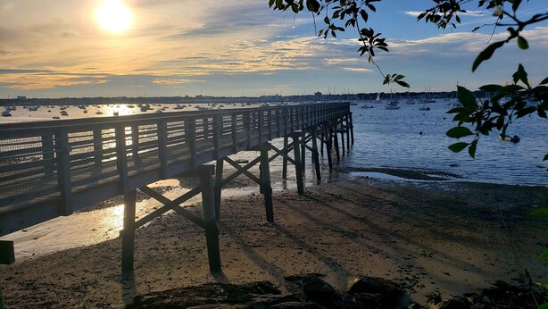 Eine Pier, die sich über einen Strand erstreckt, mit Booten im Wasser.