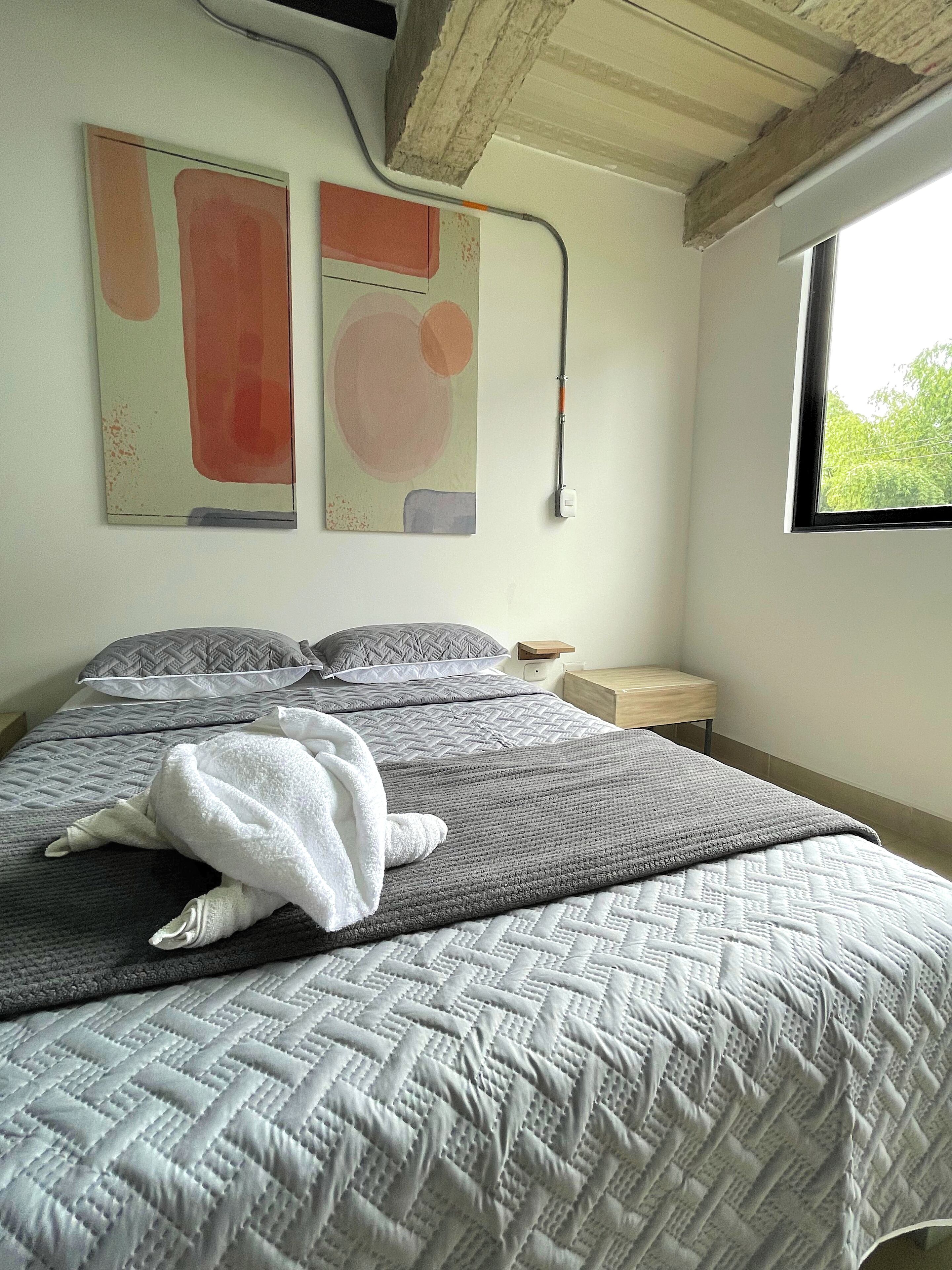 Un dormitorio con una cama, almohadas, un edredón y dos cuadros abstractos en la pared.