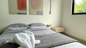 Un dormitorio con una cama, almohadas, un edredón y dos cuadros abstractos en la pared.