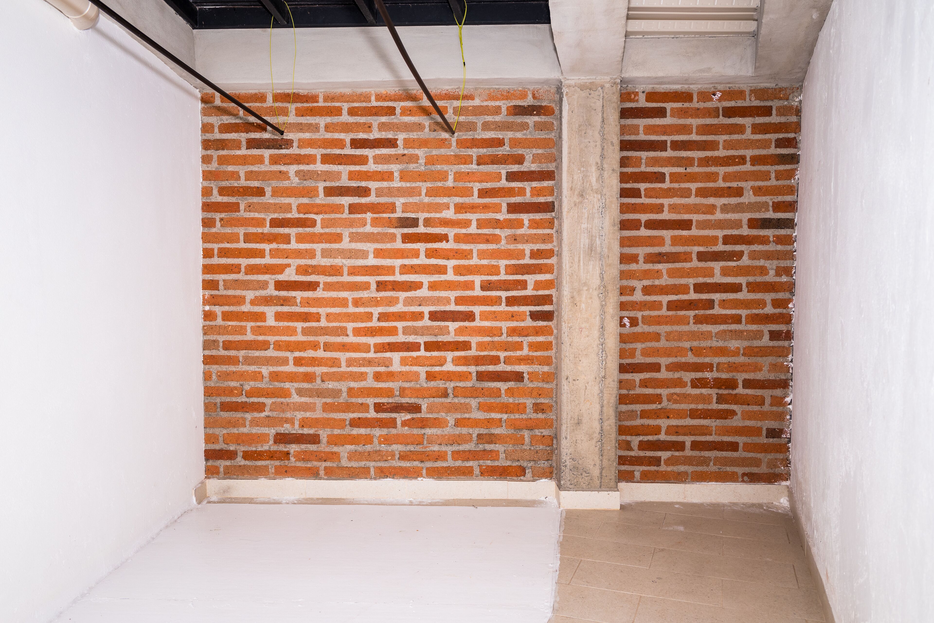 Una habitación con pared de ladrillo, suelo pintado de blanco y vigas de techo a la vista.