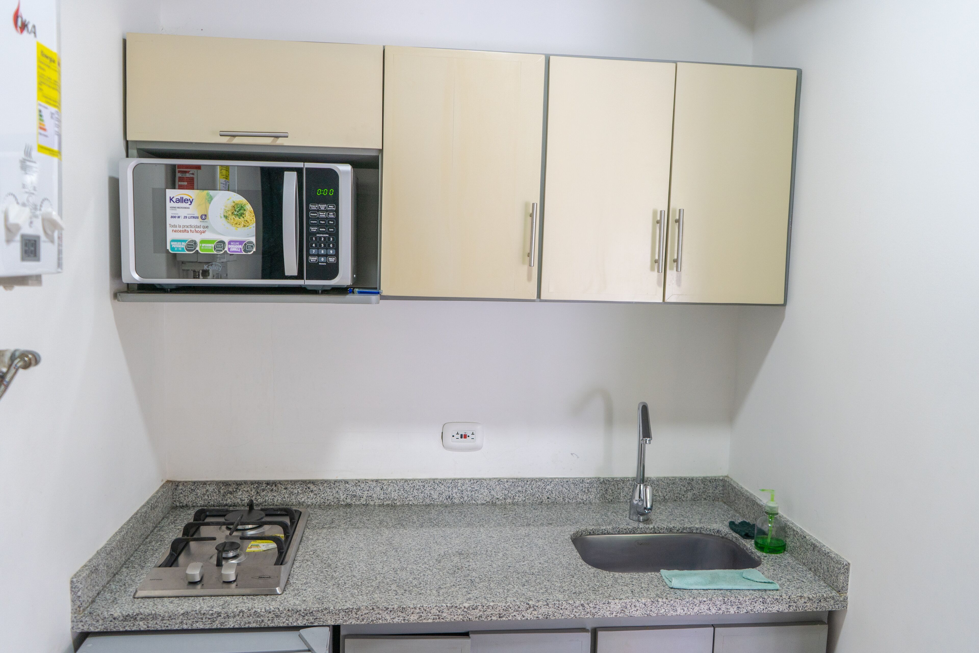 Una cocina compacta con estufa a gas, microondas, fregadero y armarios.