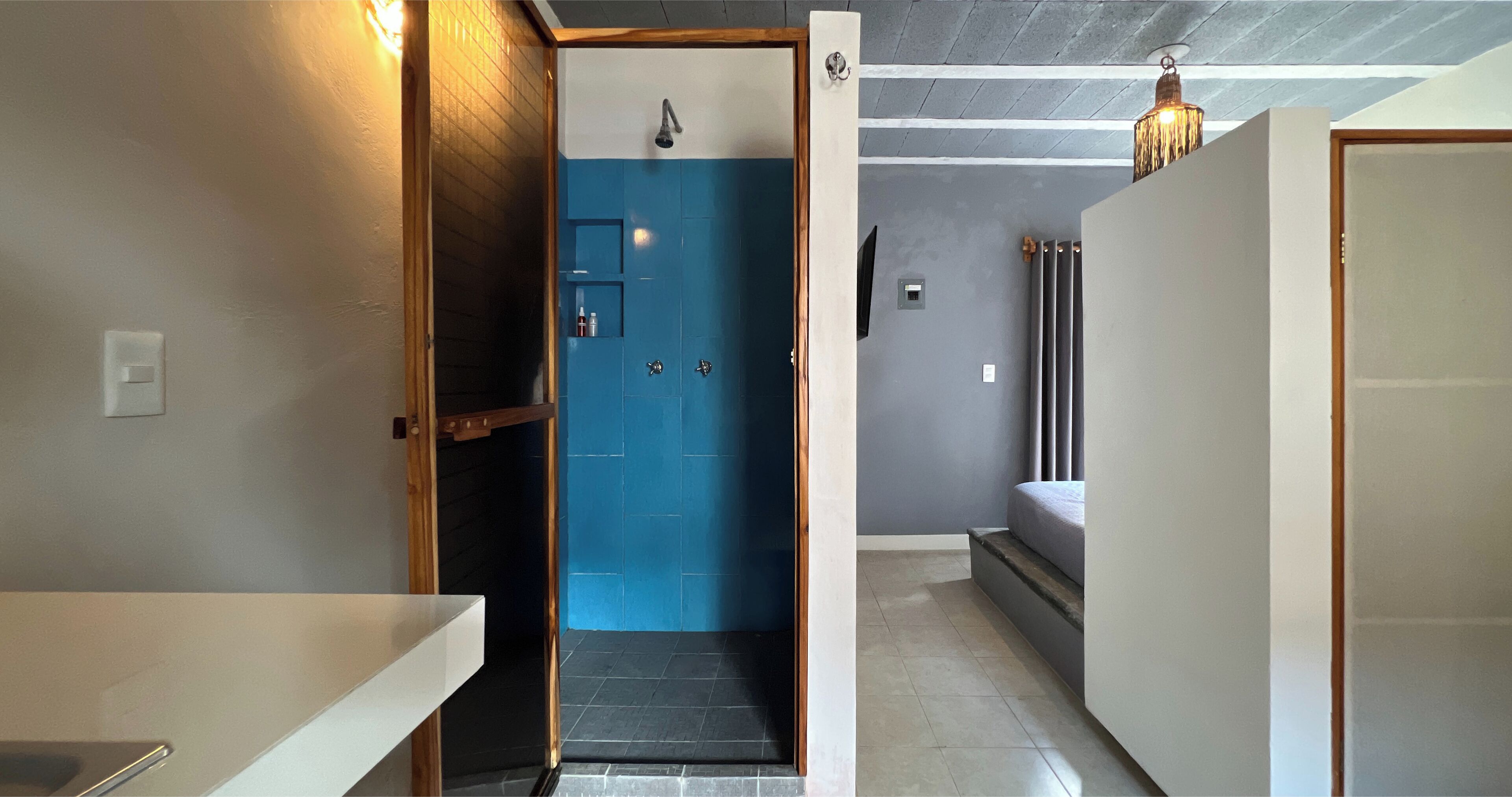 A narrow hallway with a blue door leading to a bathroom, a bed, and a radiator.