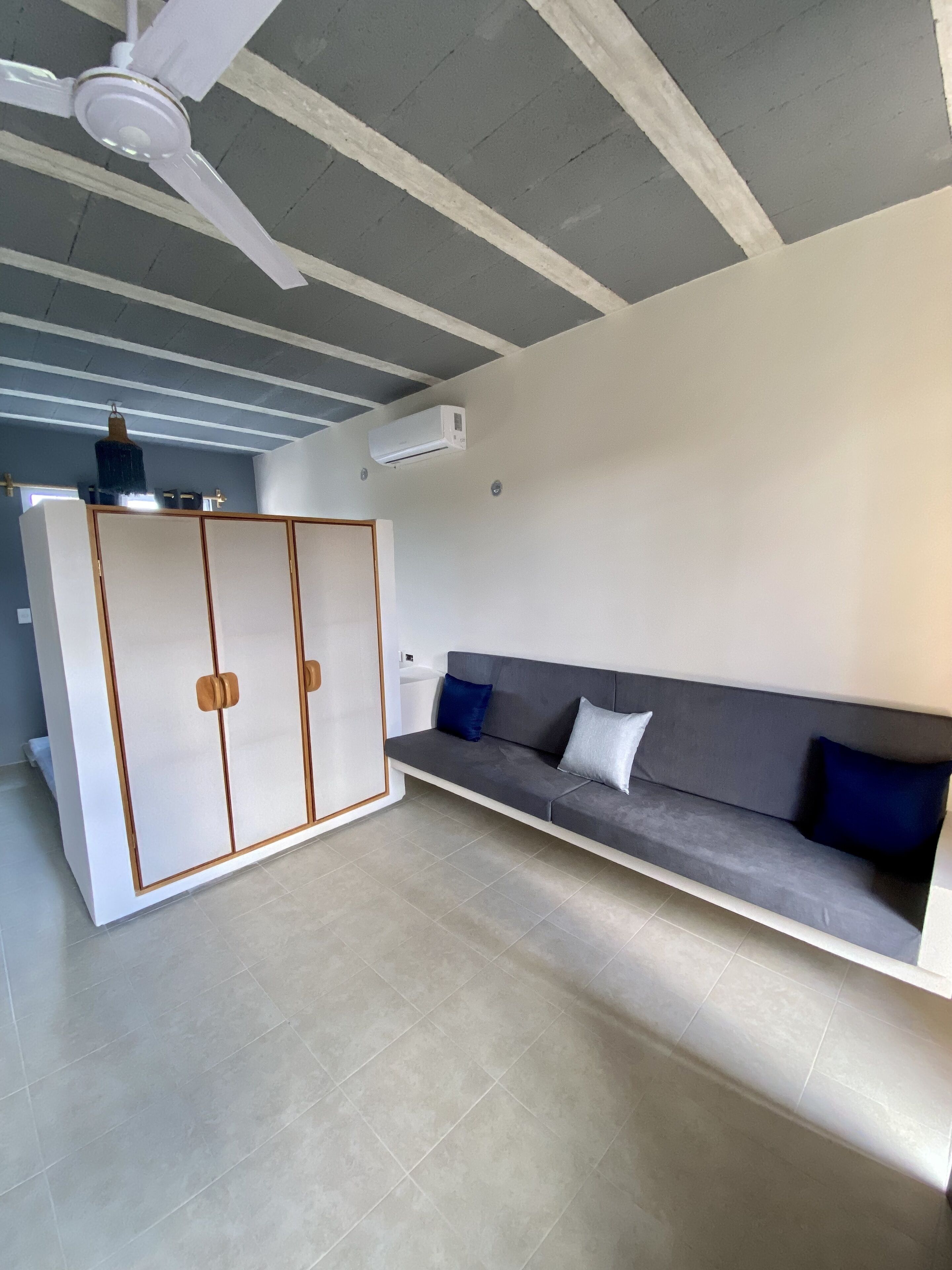 Una sala de estar moderna con un sofá gris, un armario blanco y un ventilador de techo.