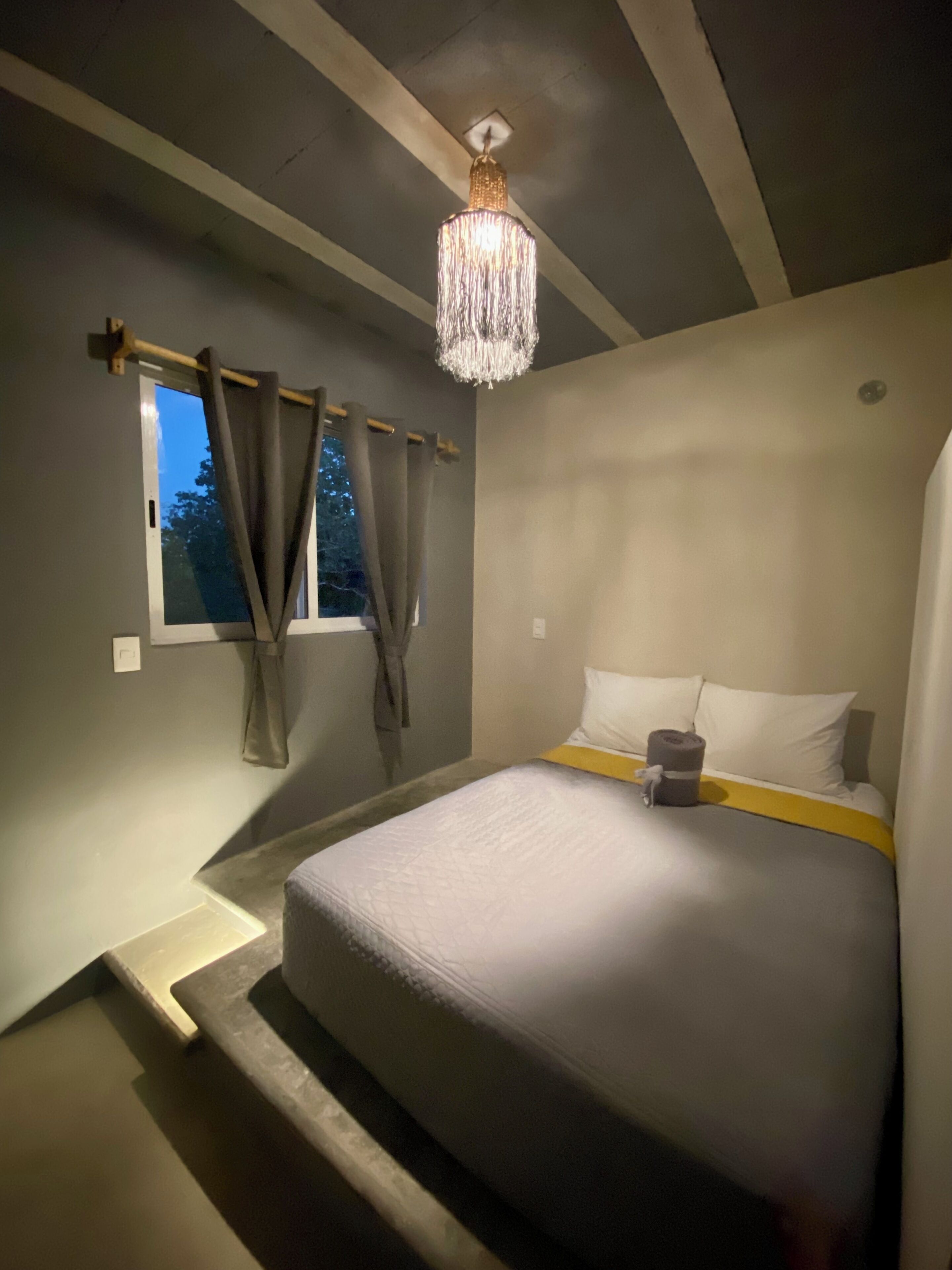 A bedroom with a bed, curtains, a chandelier, and a window.