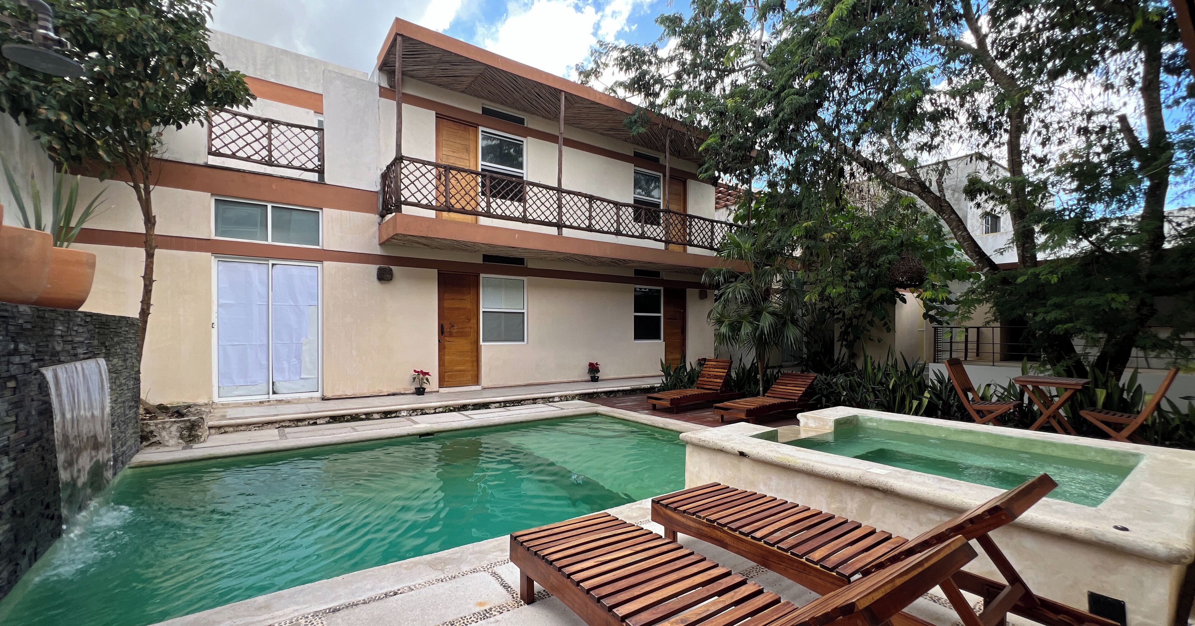 A pool area with wooden loungers, a small waterfall, and a building with a balcony.