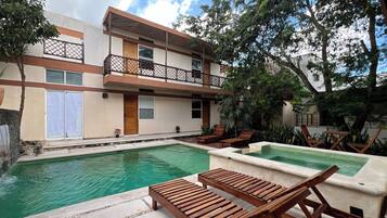 A pool area with wooden loungers, a small waterfall, and a building with a balcony.